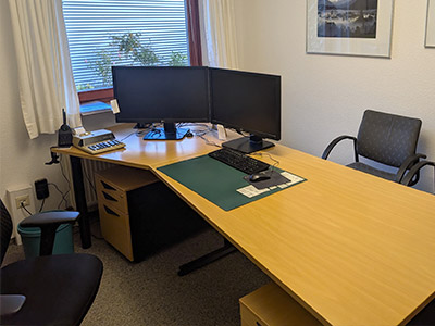 Heller Büroraum der Steuerring-Beratungsstelle Flensburg mit Eckschreibtisch, zwei Monitoren, Fenster mit Vorhängen und Pflanzen.